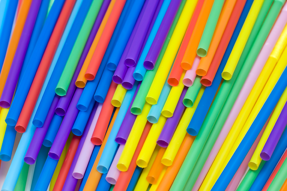 Brightly colored straws thrown around on a table. Some of them are showing the lower side of the tube, with only a few of the flexible heads visible. The colors range from blue to red tones.